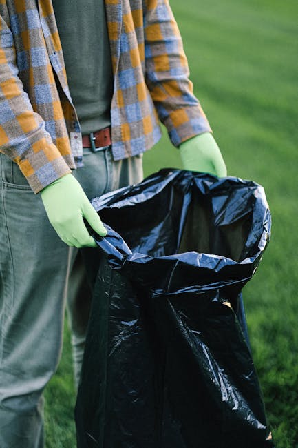 A crumpled orange plastic rubbish bag lying on a rough, dark asphalt surface in an outdoor urban setting. The bag appears to be partially open, revealing some indistinct contents inside. It is positio